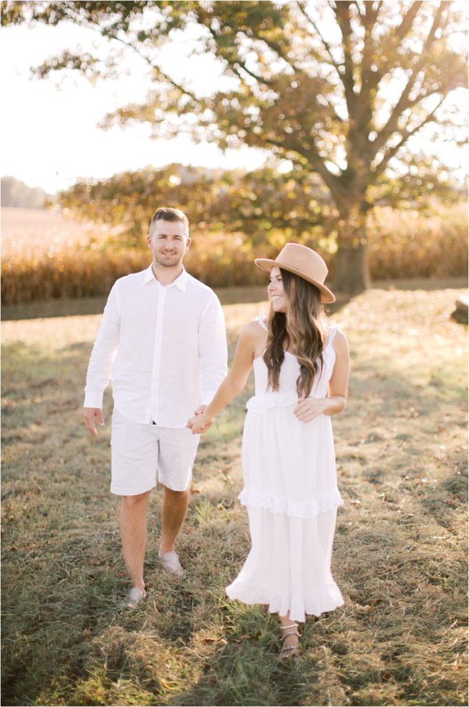 husband and wife walk through field during Hanover family session