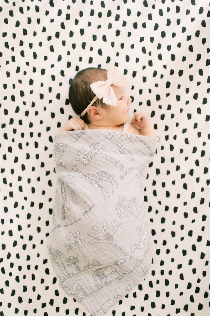 baby girl with bow on head lays on spotted sheets during newborn photos in crib