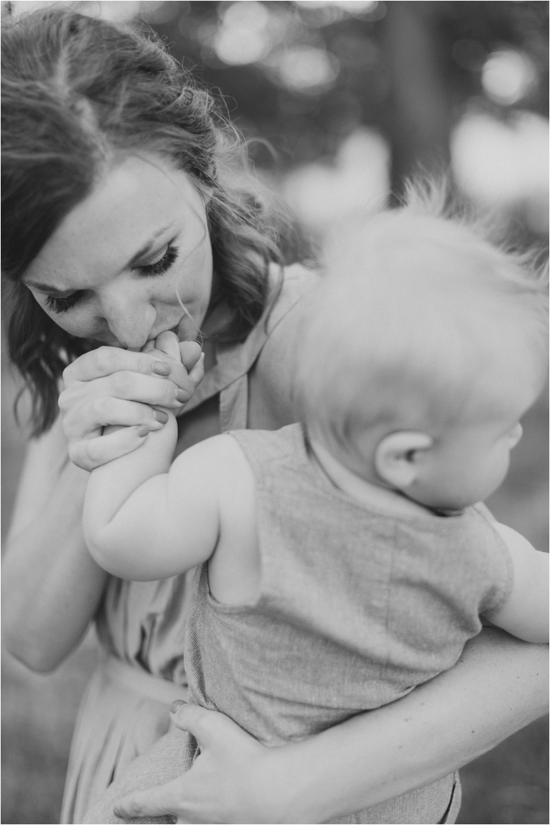 mom kisses toddler's hand during Whispering Oaks Vineyard Family Session