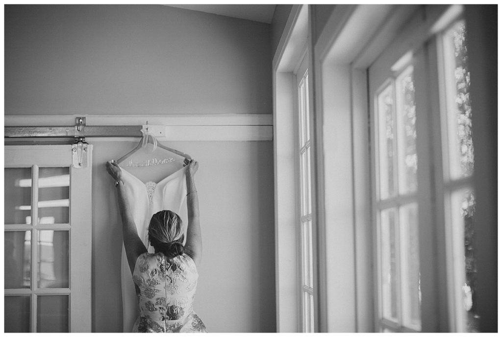black and white photo of bride hanging up her wedding dress